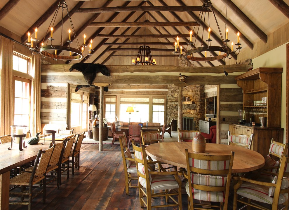 Idée de décoration pour une salle à manger ouverte sur le salon chalet de taille moyenne avec un mur beige, parquet foncé, une cheminée standard et un manteau de cheminée en pierre.