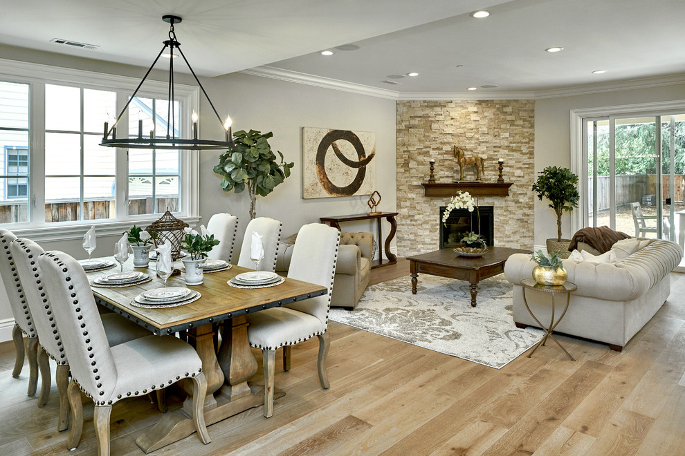 Idée de décoration pour une salle à manger ouverte sur le salon méditerranéenne de taille moyenne avec un mur gris, un sol en bois brun, une cheminée d'angle, un manteau de cheminée en pierre et un sol gris.