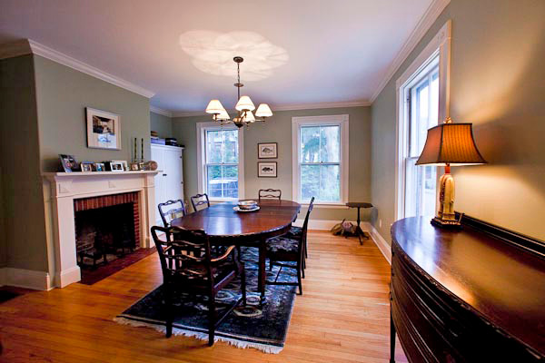 Idée de décoration pour une salle à manger tradition fermée et de taille moyenne avec un mur vert, un sol en bois brun, une cheminée standard et un manteau de cheminée en brique.