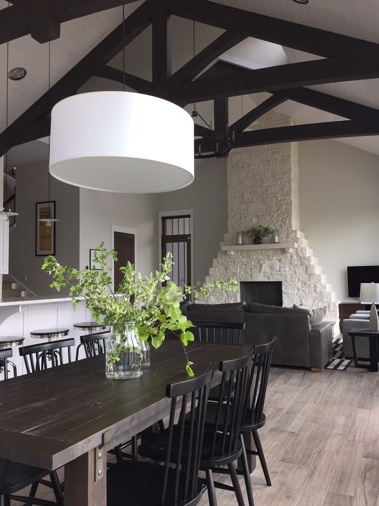 На фото: большая гостиная-столовая в современном стиле с белыми стенами, полом из керамической плитки, стандартным камином, фасадом камина из камня и коричневым полом