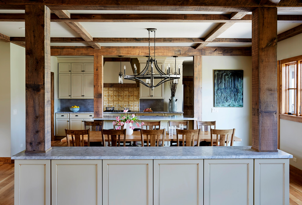 Ispirazione per una sala da pranzo aperta verso la cucina stile rurale di medie dimensioni con pareti beige, parquet chiaro, pavimento marrone e travi a vista