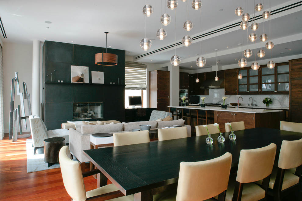 Cette image montre une salle à manger ouverte sur le salon design de taille moyenne avec un mur blanc, un sol en bois brun, une cheminée standard et un manteau de cheminée en béton.