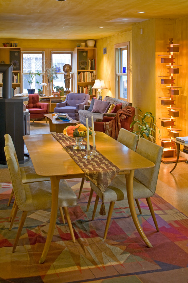 Foto di una piccola sala da pranzo aperta verso il soggiorno minimalista con pareti gialle, stufa a legna, pavimento in sughero, cornice del camino in pietra e pavimento marrone