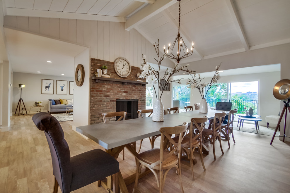 Idée de décoration pour une grande salle à manger ouverte sur la cuisine champêtre avec un mur blanc, une cheminée double-face, un manteau de cheminée en brique, un sol en bois brun et éclairage.