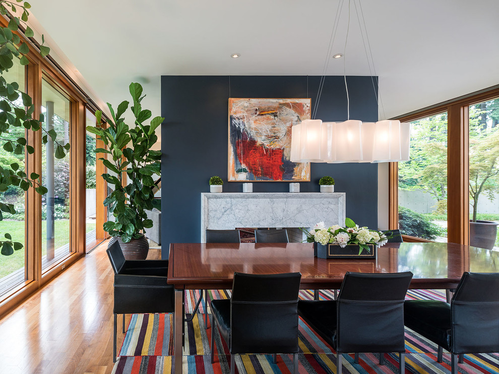 Réalisation d'une salle à manger design avec un mur bleu, un sol en bois brun, une cheminée double-face et un manteau de cheminée en pierre.