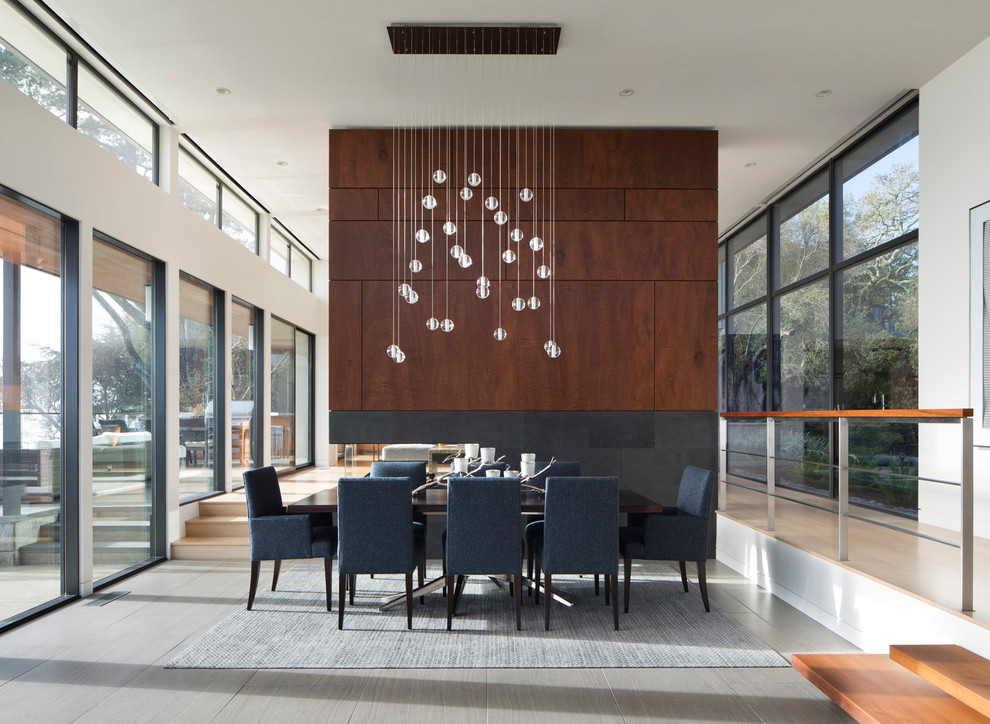 Идея дизайна: большая гостиная-столовая в стиле модернизм с белыми стенами, полом из керамогранита, двусторонним камином, фасадом камина из камня и серым полом