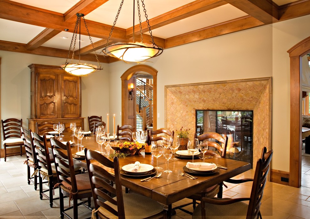 Exemple d'une grande salle à manger chic fermée avec un mur beige, un sol en calcaire, une cheminée double-face, un manteau de cheminée en carrelage et un sol beige.