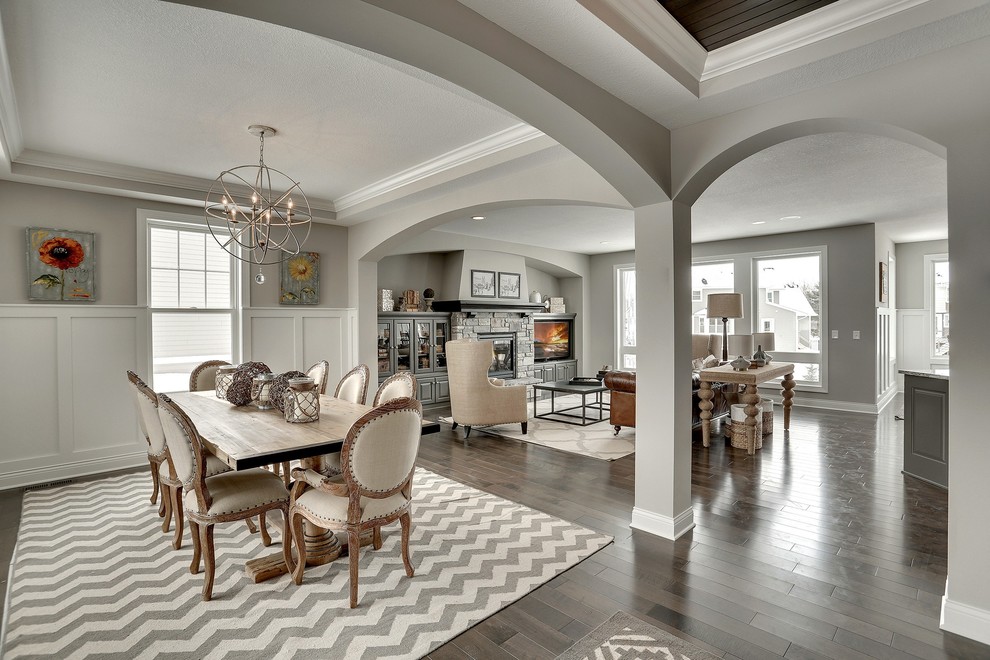 Inspiration pour une grande salle à manger ouverte sur le salon traditionnelle avec un mur gris, une cheminée standard, un manteau de cheminée en pierre et éclairage.