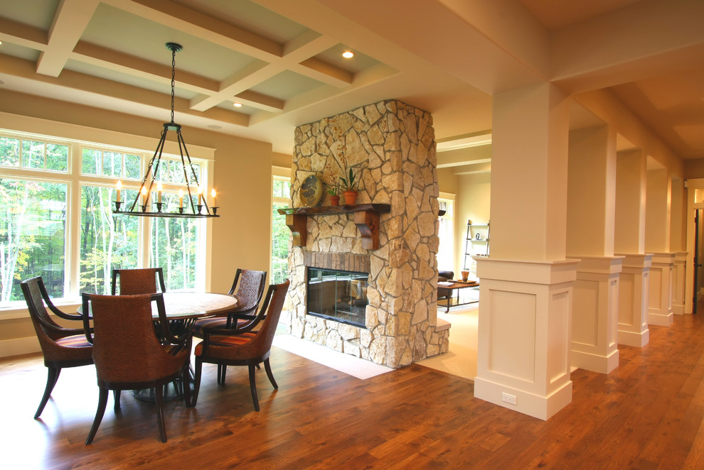 Exemple d'une salle à manger chic avec un mur beige, une cheminée double-face, un manteau de cheminée en pierre et un sol en bois brun.