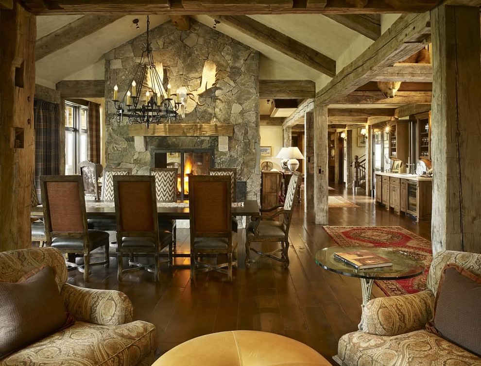 Exemple d'une grande salle à manger ouverte sur le salon montagne avec un mur beige, un sol en bois brun, une cheminée double-face et un manteau de cheminée en pierre.