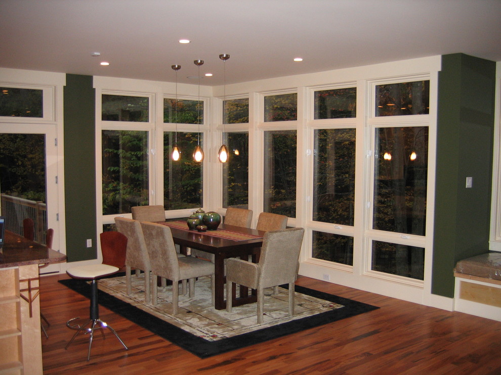 Cette image montre une salle à manger ouverte sur la cuisine design de taille moyenne avec un mur vert et un sol en bois brun.