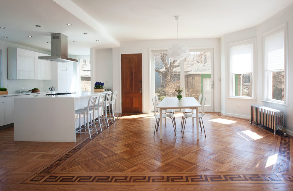 Réalisation d'une salle à manger ouverte sur la cuisine design avec un mur blanc et un sol en bois brun.