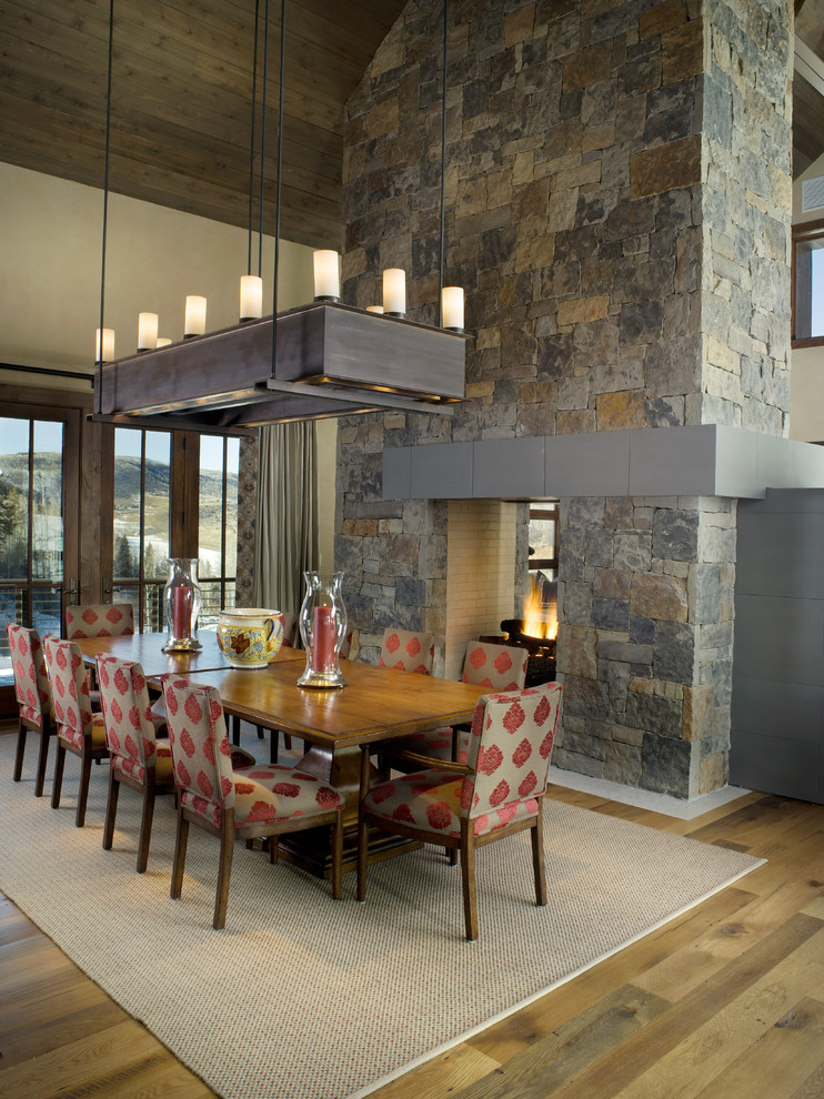 Aménagement d'une grande salle à manger ouverte sur la cuisine montagne avec un mur beige, un sol en bois brun, une cheminée double-face et un manteau de cheminée en pierre.