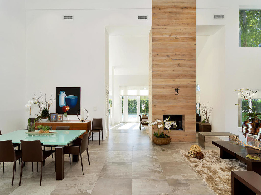 На фото: огромная гостиная-столовая в стиле модернизм с белыми стенами, полом из керамогранита, стандартным камином, фасадом камина из плитки и серым полом с