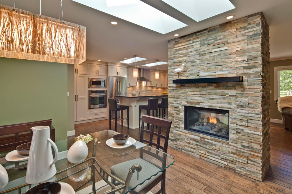 Cette image montre une salle à manger ouverte sur le salon design de taille moyenne avec un mur vert, un sol en bois brun, une cheminée double-face et un manteau de cheminée en pierre.