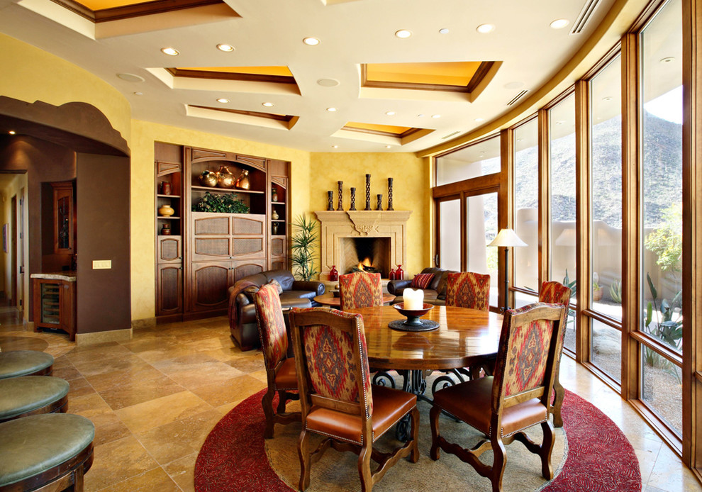 Aménagement d'une grande salle à manger ouverte sur la cuisine sud-ouest américain avec un mur jaune, un sol en carrelage de céramique, une cheminée standard, un manteau de cheminée en pierre et éclairage.