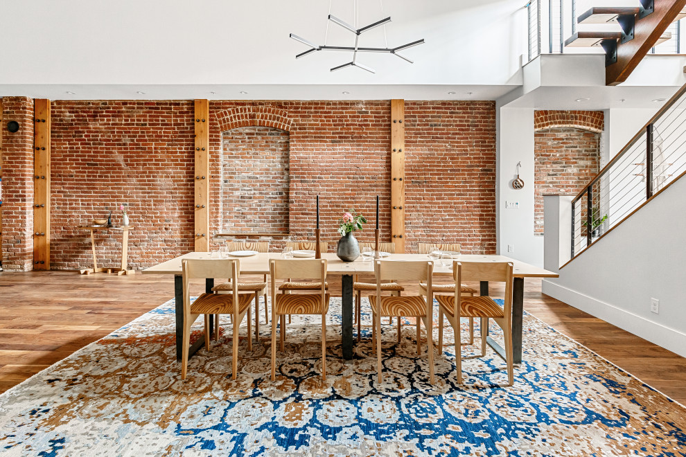 Idee per una sala da pranzo aperta verso il soggiorno industriale con pareti rosse, pavimento in legno massello medio, pavimento marrone e pareti in mattoni