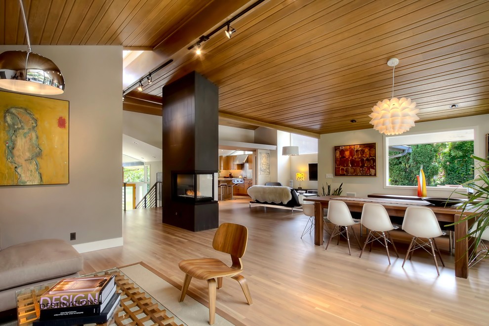 Immagine di una sala da pranzo aperta verso il soggiorno minimalista con camino bifacciale e pareti beige