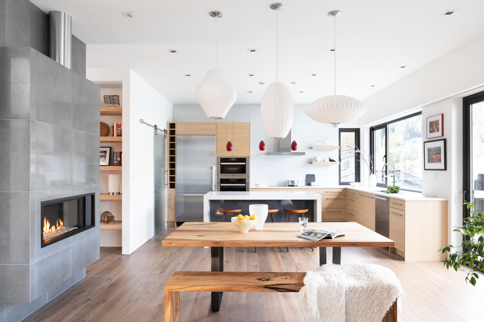 Cette image montre une grande salle à manger ouverte sur la cuisine design avec un sol en bois brun, un mur blanc, une cheminée ribbon, un manteau de cheminée en béton et un sol marron.