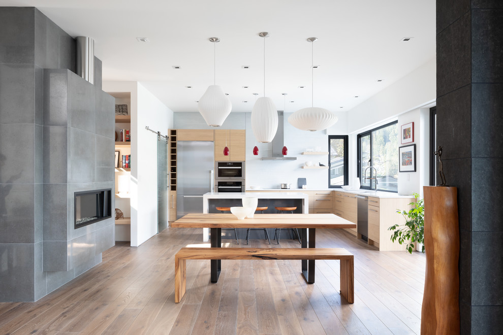 Große Moderne Wohnküche mit weißer Wandfarbe, braunem Holzboden, Tunnelkamin, gefliester Kaminumrandung und braunem Boden in Vancouver