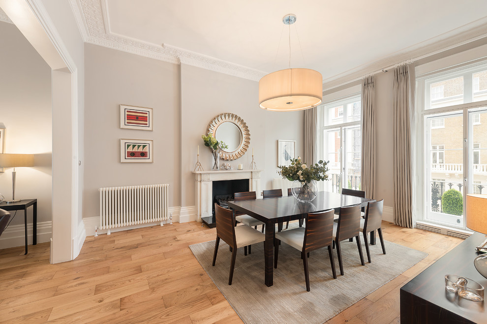 Inspiration for a classic dining room in London with grey walls, light hardwood flooring, a standard fireplace, beige floors and feature lighting.