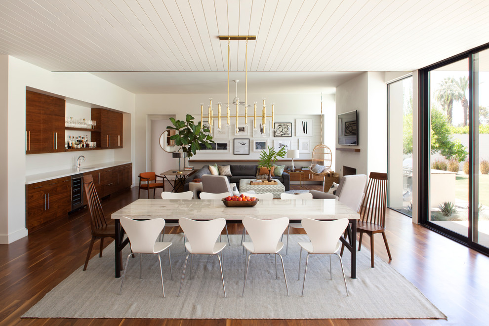 Cette image montre une grande salle à manger ouverte sur le salon vintage avec un mur blanc et un sol en bois brun.