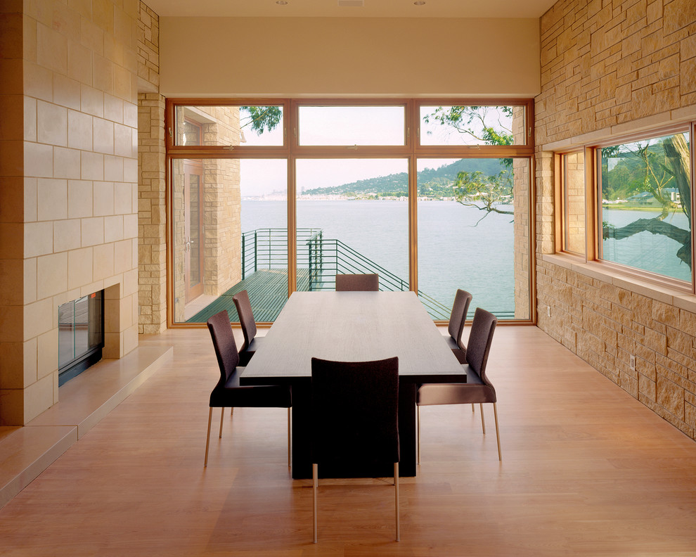 Exemple d'une salle à manger ouverte sur la cuisine tendance de taille moyenne avec un sol en bois brun, une cheminée double-face, un manteau de cheminée en pierre et un sol marron.