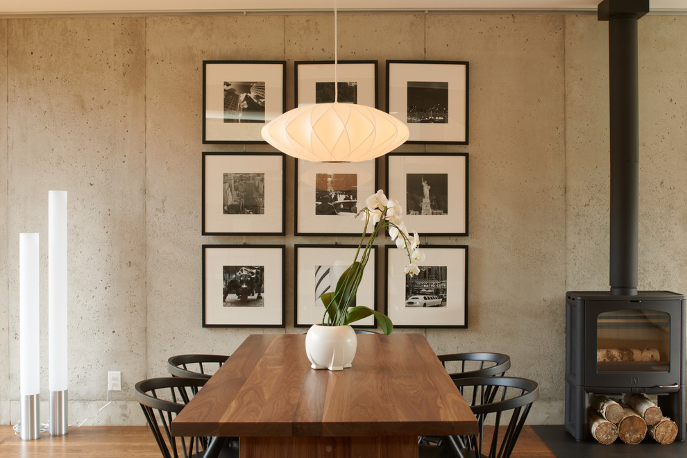Foto de comedor contemporáneo con paredes grises, suelo de madera oscura, estufa de leña y cuadros