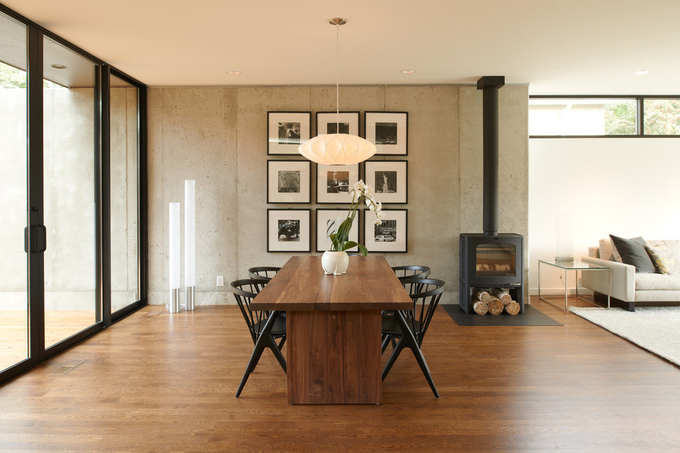 Imagen de comedor minimalista abierto con suelo de madera oscura, estufa de leña y cuadros