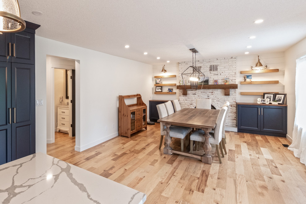 Große Rustikale Wohnküche mit weißer Wandfarbe, braunem Holzboden, Kamin, Kaminumrandung aus Backstein, braunem Boden und Holzdielenwänden in Edmonton