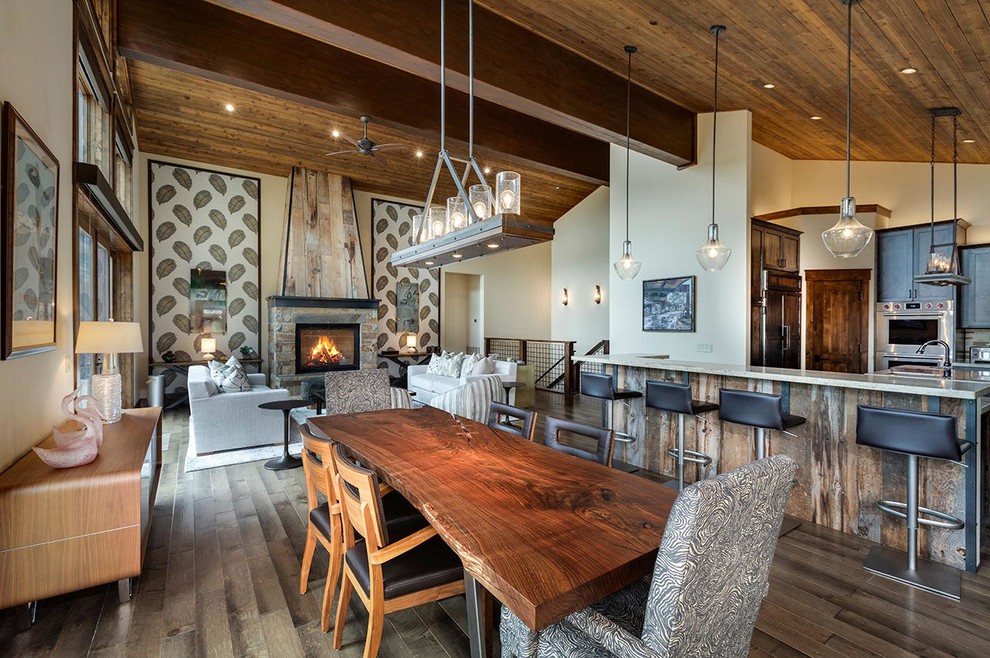Idée de décoration pour une grande salle à manger ouverte sur le salon chalet avec un mur beige, un sol en bois brun, un poêle à bois, un manteau de cheminée en pierre et un sol marron.