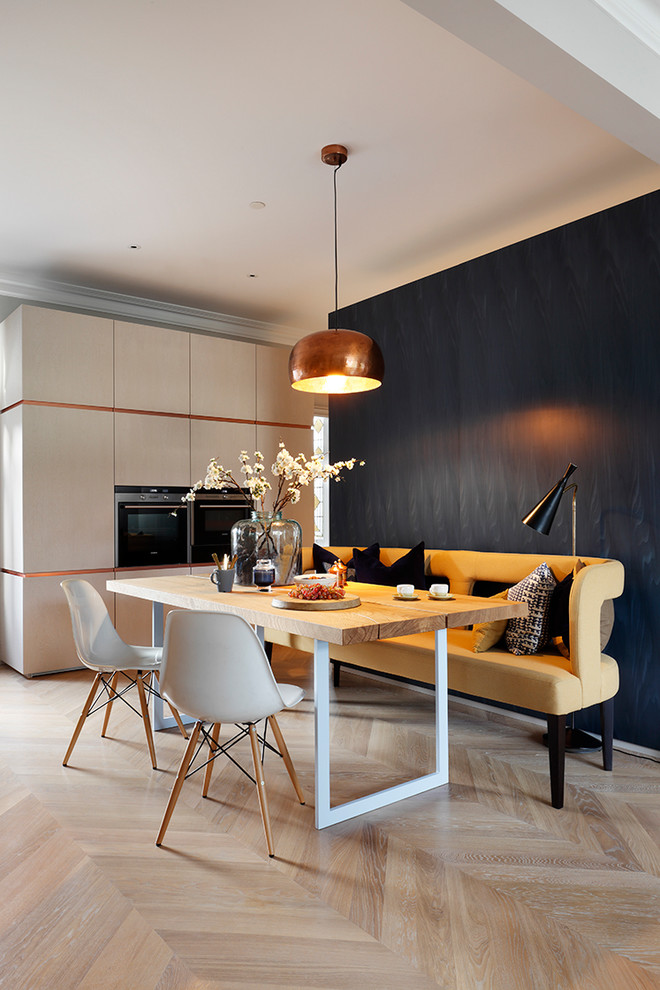 This is an example of a contemporary kitchen/dining room in London with black walls, light hardwood flooring and feature lighting.