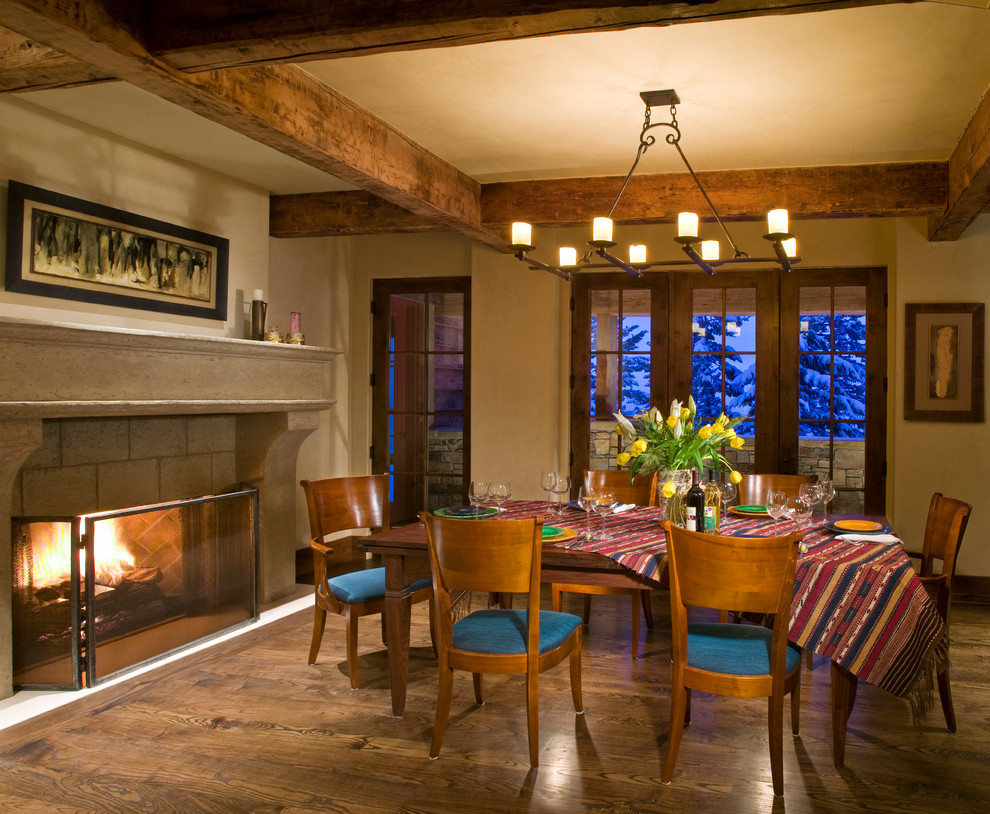 Idée de décoration pour une grande salle à manger chalet fermée avec un sol en bois brun, une cheminée standard et un mur beige.