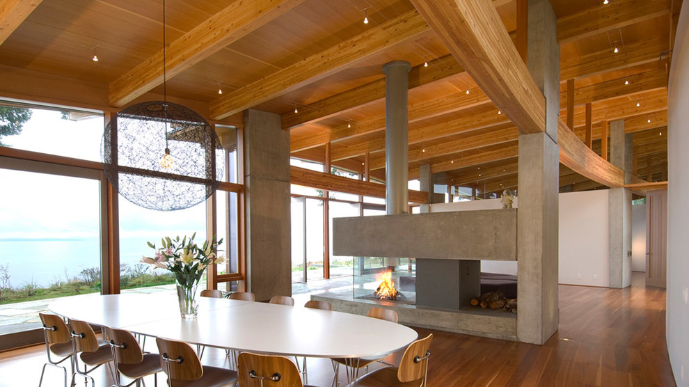 This is an example of a contemporary kitchen/dining room in Vancouver with white walls, medium hardwood flooring, a two-sided fireplace and a concrete fireplace surround.