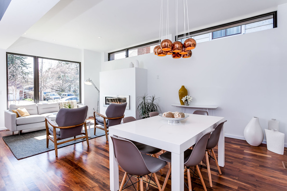 Cette photo montre une salle à manger ouverte sur le salon tendance de taille moyenne avec un mur blanc, un sol en bois brun, une cheminée ribbon et un manteau de cheminée en métal.