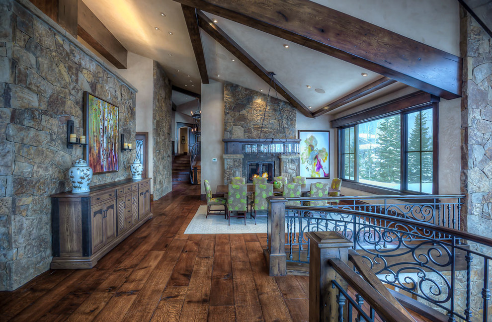 Cette photo montre une très grande salle à manger ouverte sur la cuisine montagne avec un mur beige, un sol en bois brun, une cheminée double-face et un manteau de cheminée en pierre.