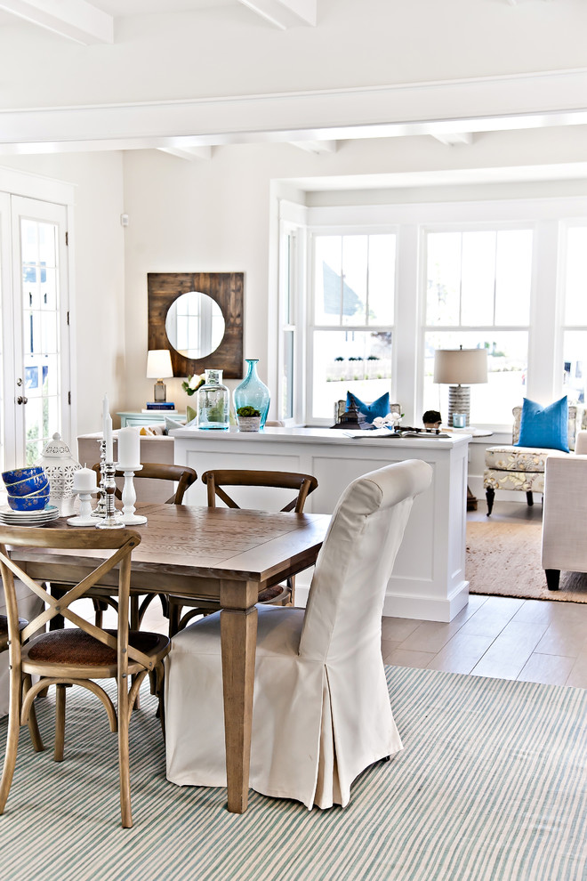Aménagement d'une salle à manger ouverte sur la cuisine bord de mer de taille moyenne avec un mur blanc, parquet clair et un sol beige.