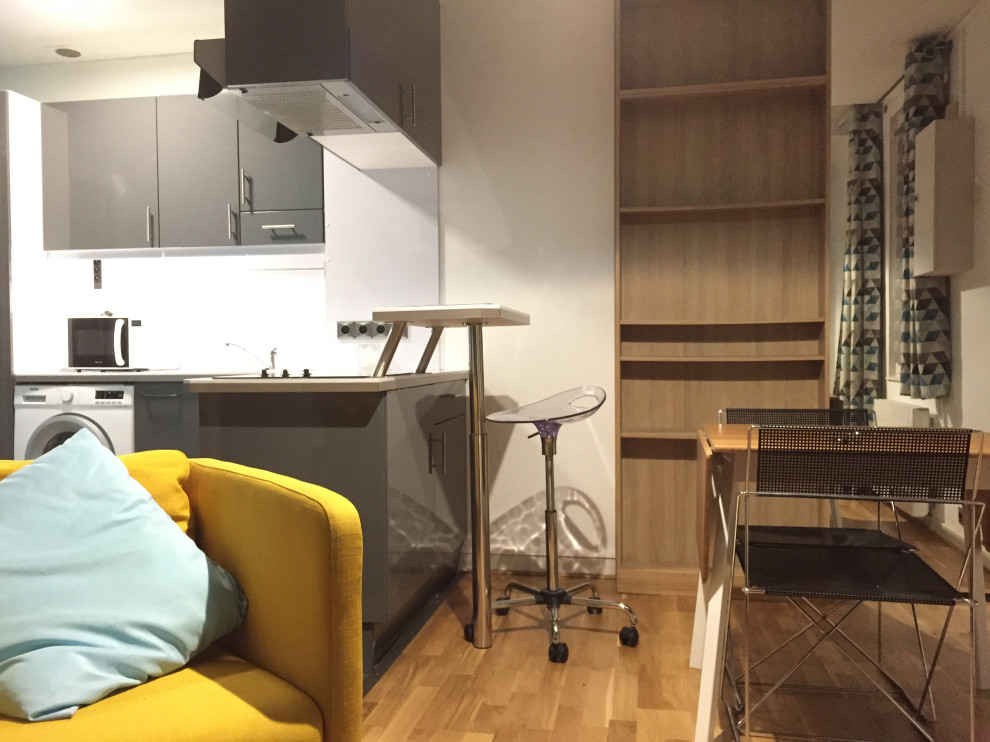 Kleine Moderne Wohnküche ohne Kamin mit weißer Wandfarbe, hellem Holzboden und braunem Boden in Paris