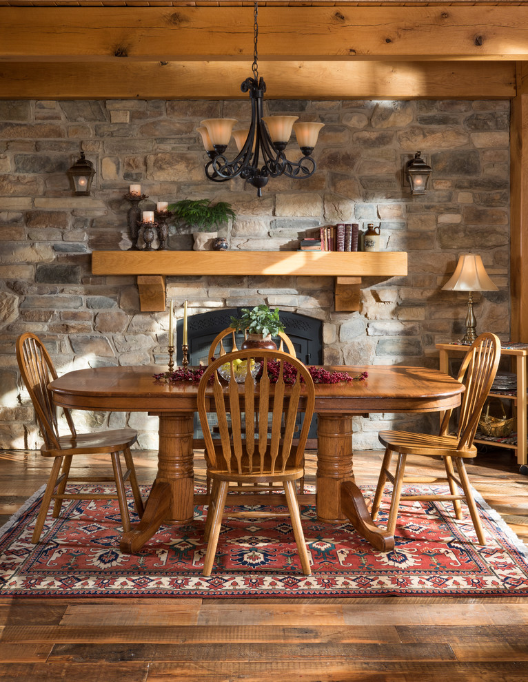 Inspiration pour une salle à manger ouverte sur la cuisine traditionnelle avec un sol en bois brun, un mur gris, une cheminée standard et un manteau de cheminée en pierre.