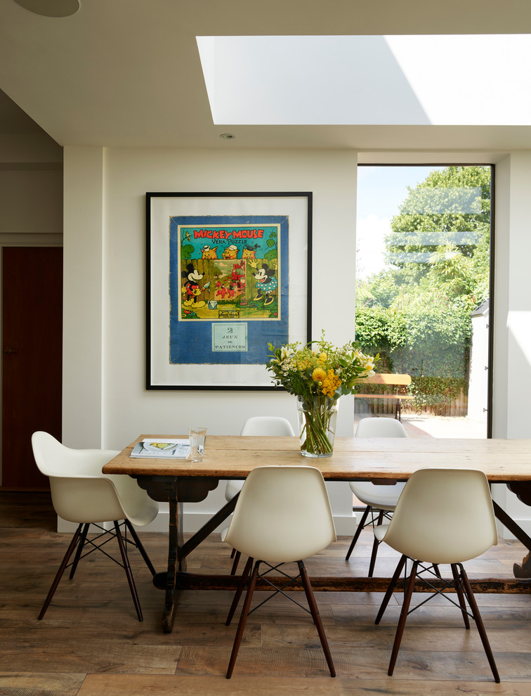 Cette photo montre une grande salle à manger ouverte sur la cuisine tendance avec un sol marron, un mur blanc et un sol en bois brun.