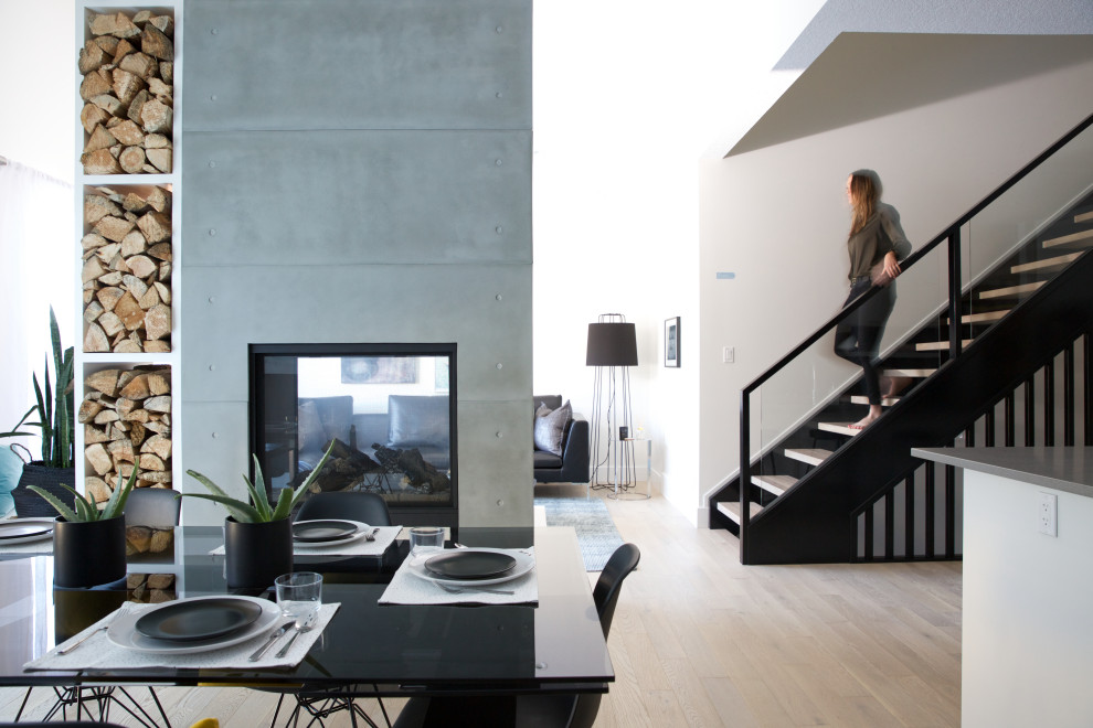 На фото: кухня-столовая среднего размера в скандинавском стиле с черными стенами, светлым паркетным полом, двусторонним камином, фасадом камина из бетона, коричневым полом и сводчатым потолком