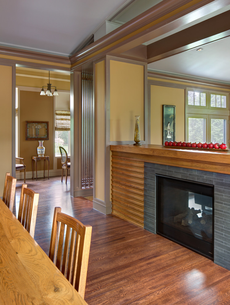 Cette photo montre une grande salle à manger ouverte sur la cuisine chic avec un mur beige, un sol en bois brun, une cheminée standard et un manteau de cheminée en pierre.