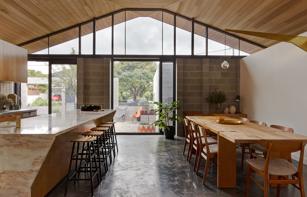 Foto di una sala da pranzo aperta verso la cucina minimal con pareti bianche, pavimento in cemento e nessun camino
