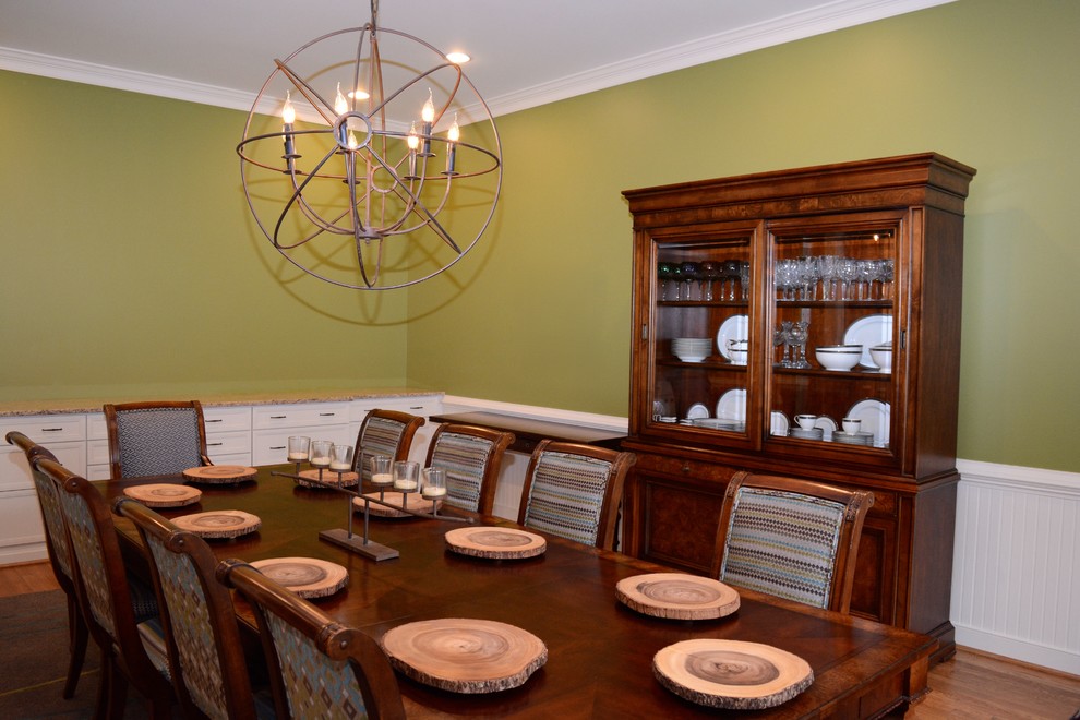 Réalisation d'une grande salle à manger ouverte sur la cuisine champêtre avec un mur vert, un sol en bois brun et un manteau de cheminée en pierre.