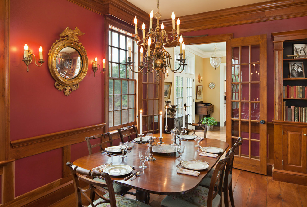 Idées déco pour une grande salle à manger ouverte sur le salon campagne avec un mur rouge, un sol en bois brun, une cheminée standard et un manteau de cheminée en brique.