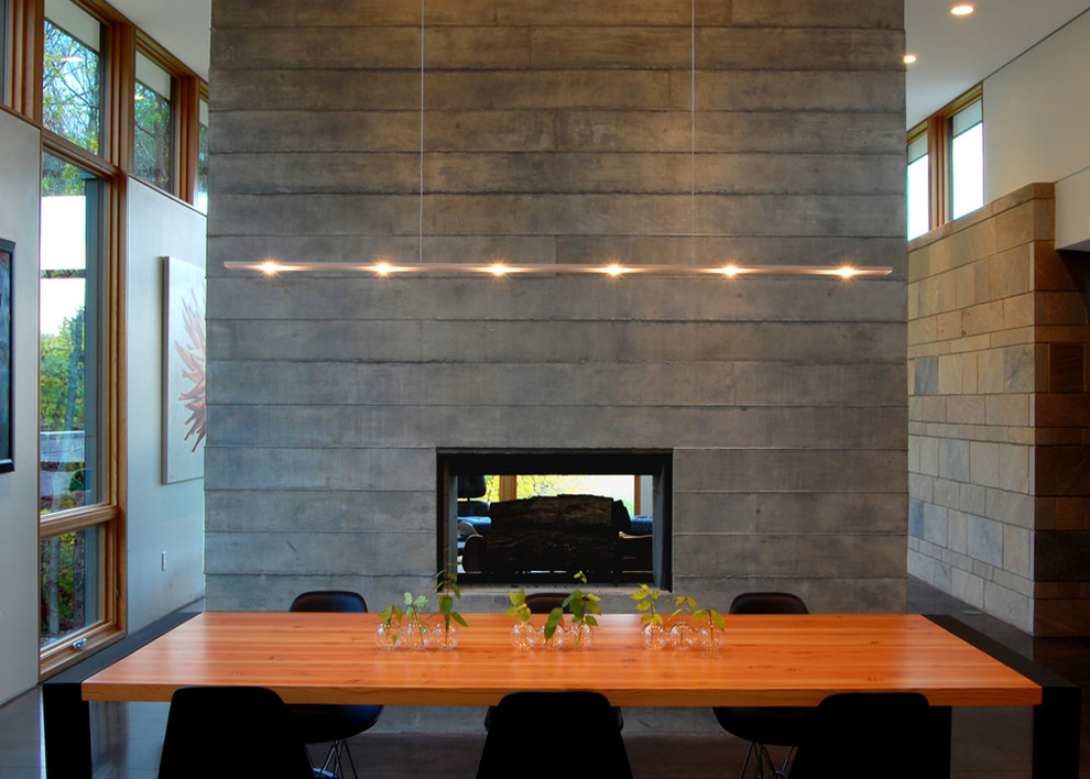 Пример оригинального дизайна: гостиная-столовая среднего размера в стиле модернизм с бетонным полом, двусторонним камином, фасадом камина из бетона, белыми стенами и коричневым полом