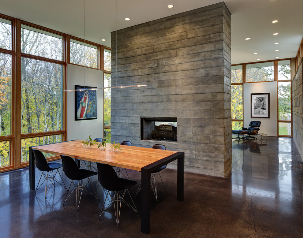 Идея дизайна: гостиная-столовая среднего размера в современном стиле с двусторонним камином, белыми стенами, бетонным полом и коричневым полом