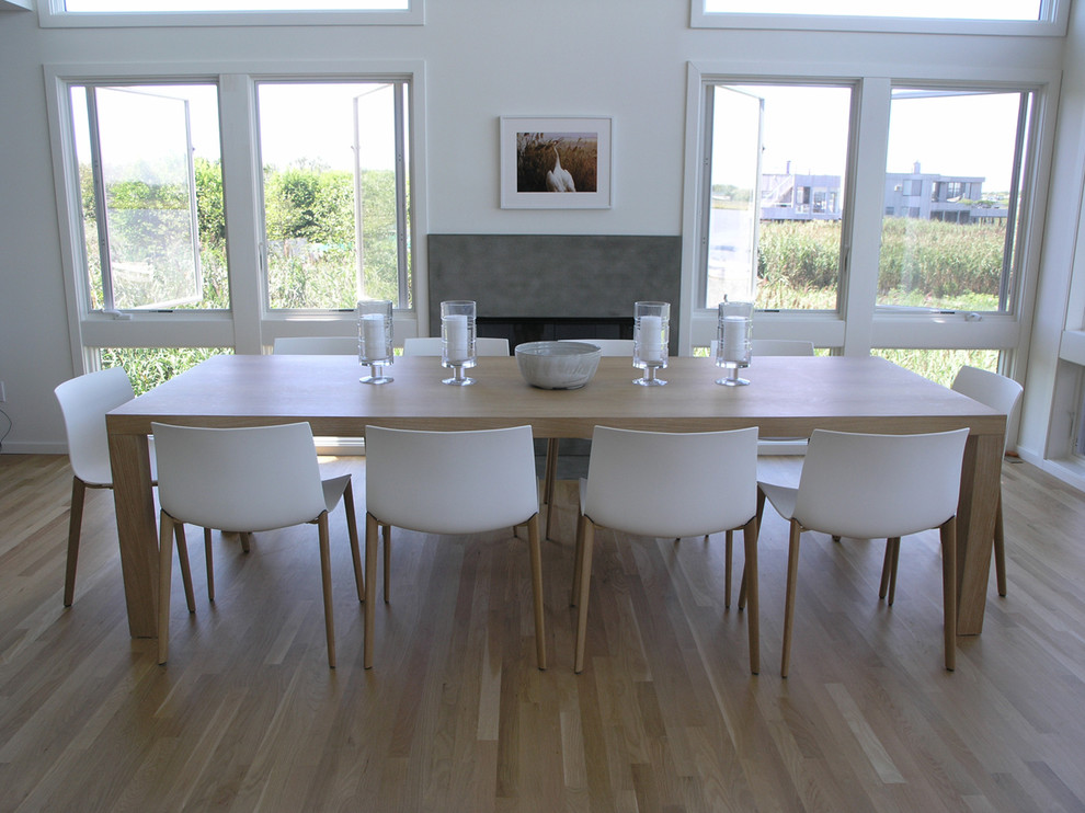 Cette photo montre une grande salle à manger tendance avec un mur blanc, parquet clair, une cheminée standard et un manteau de cheminée en pierre.