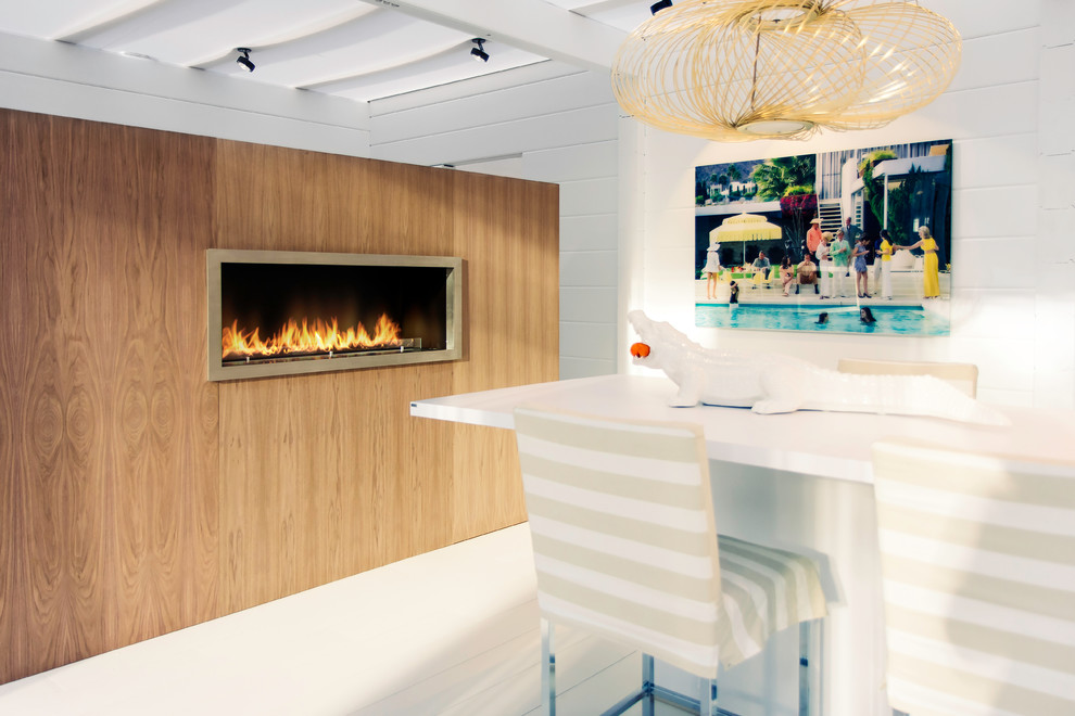 На фото: кухня-столовая среднего размера в стиле фьюжн с горизонтальным камином, фасадом камина из дерева, белыми стенами и деревянным полом с