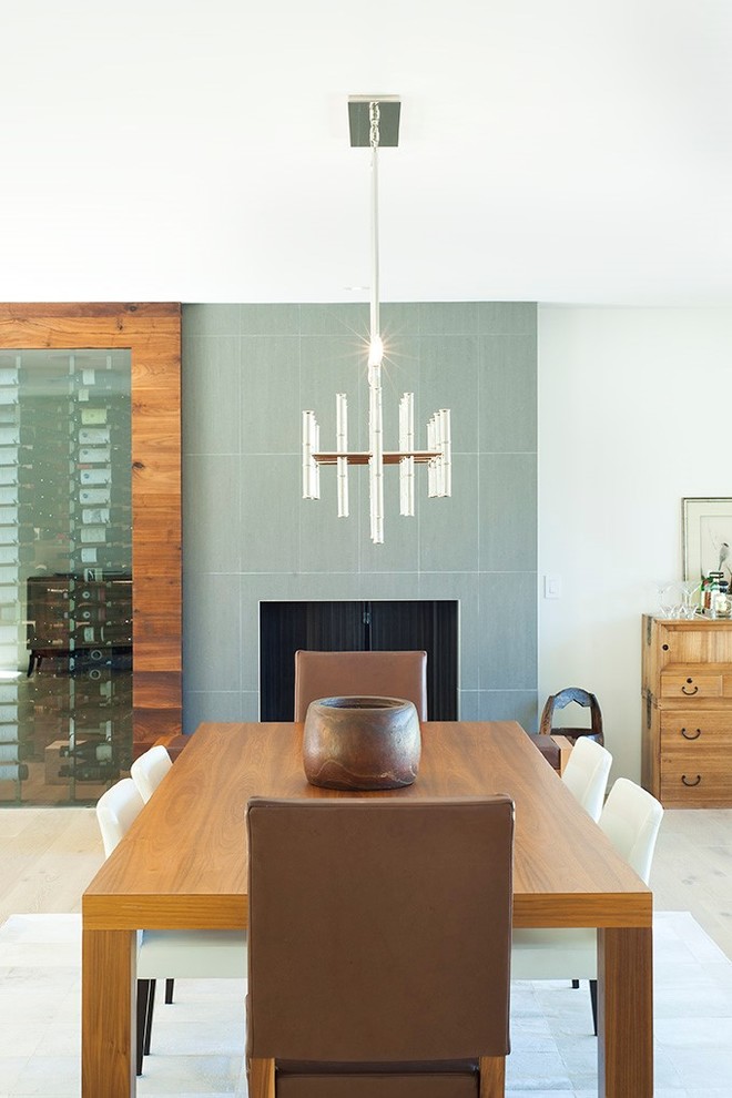 Aménagement d'une salle à manger ouverte sur le salon contemporaine de taille moyenne avec parquet clair, un manteau de cheminée en carrelage, un mur gris et une cheminée standard.
